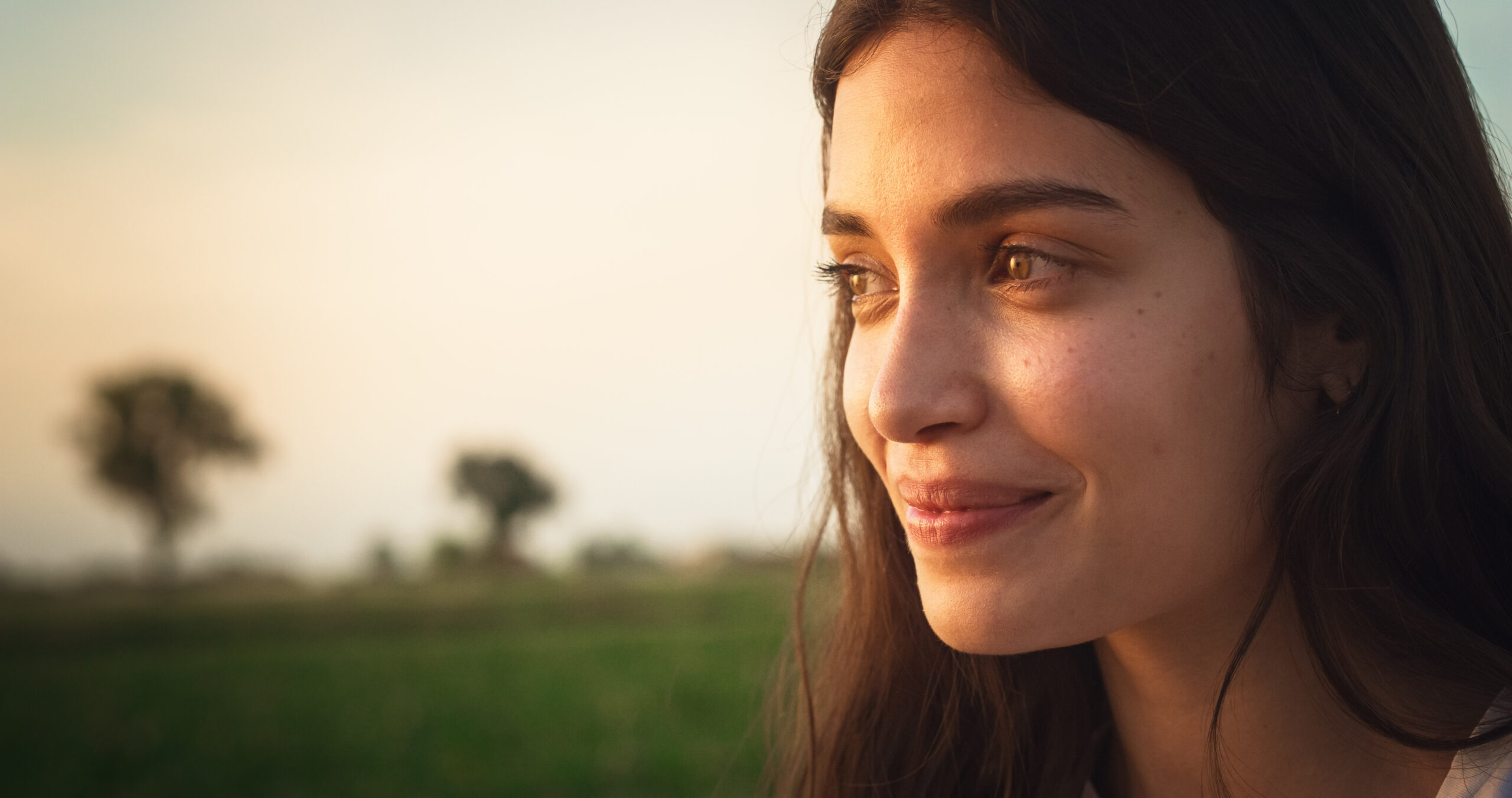 woman smiling as she looks at the sunset in a natural outdoor setting