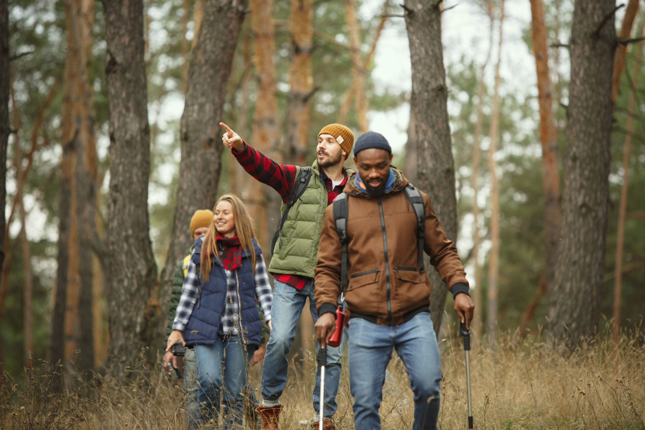 Group of friends on a camping or hiking trip in autumn day. Men and women with touristic backpacks going through the forest, talking, laughing.